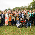 Das Team des Programm-Departments von Licht für die Welt steht zusammen auf einer grünen Wiese und lächelt in die Kamera und hebt die Hände.