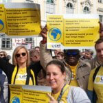 Fuenf Mitarbeiter*innen in gelben T-Shirts halten Schilder auf der Inklusions_Demo hoch. 