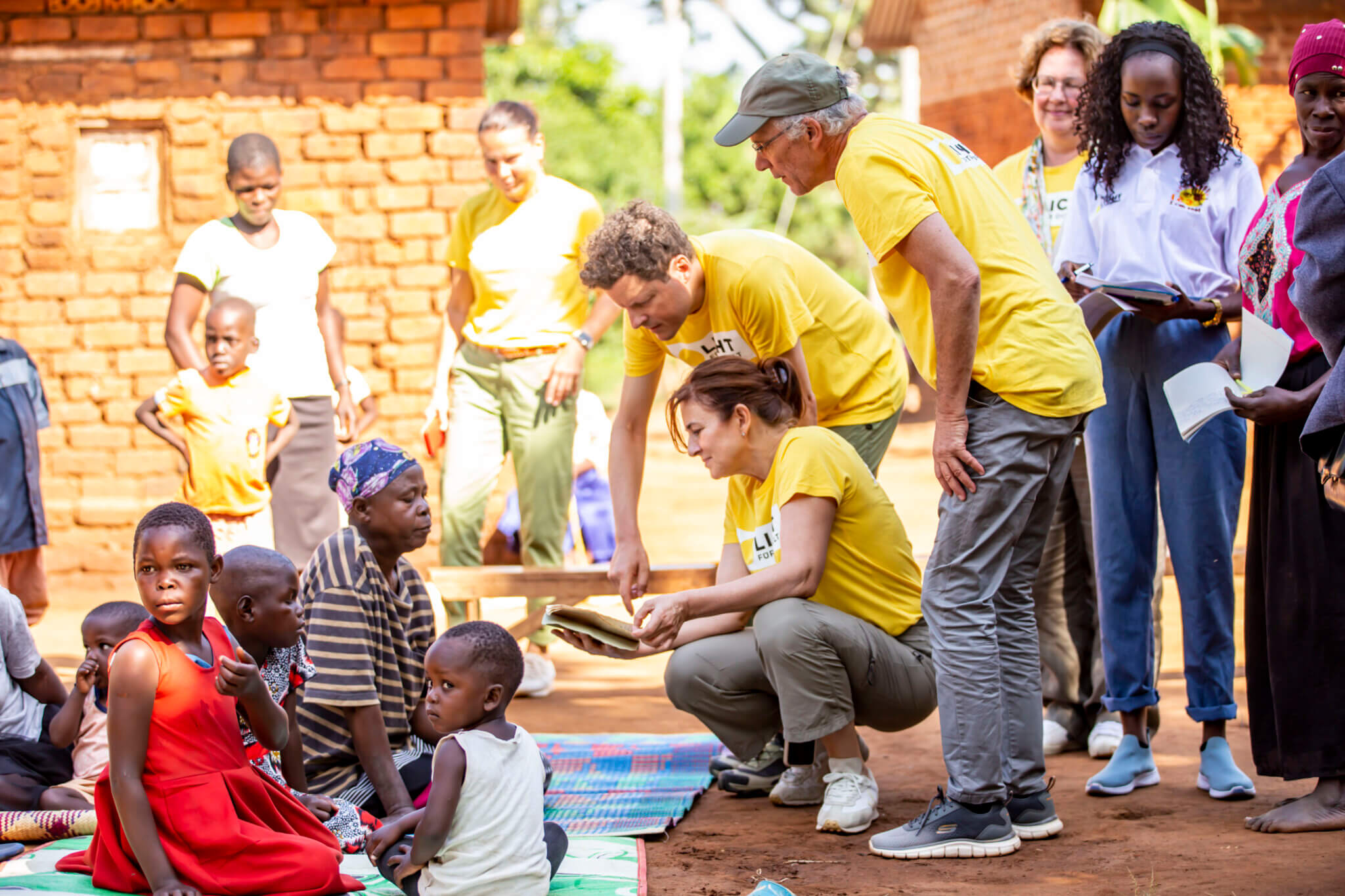 Auf dem Bild sind viele verschiedene Menschen zu sehen, ein paar davon sitzen auf dem Boden. Das Bild wurde im Dorf Kikubo in Uganda aufgenommen und entstand im Rahmen einer Reise von Augenärztinnen und -ärzten gemeinsam mit Licht für die Welt.
