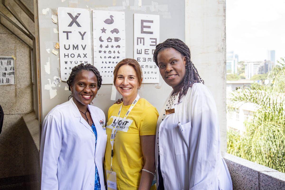 Auf dem Bild sind drei Frauen zu sehen. Zwei davon sind Ärztinnen in einer Augenklinik in Uganda. Die dritte Frau ist Augenärztin in Wien. Sie lächeln in die Kamera.