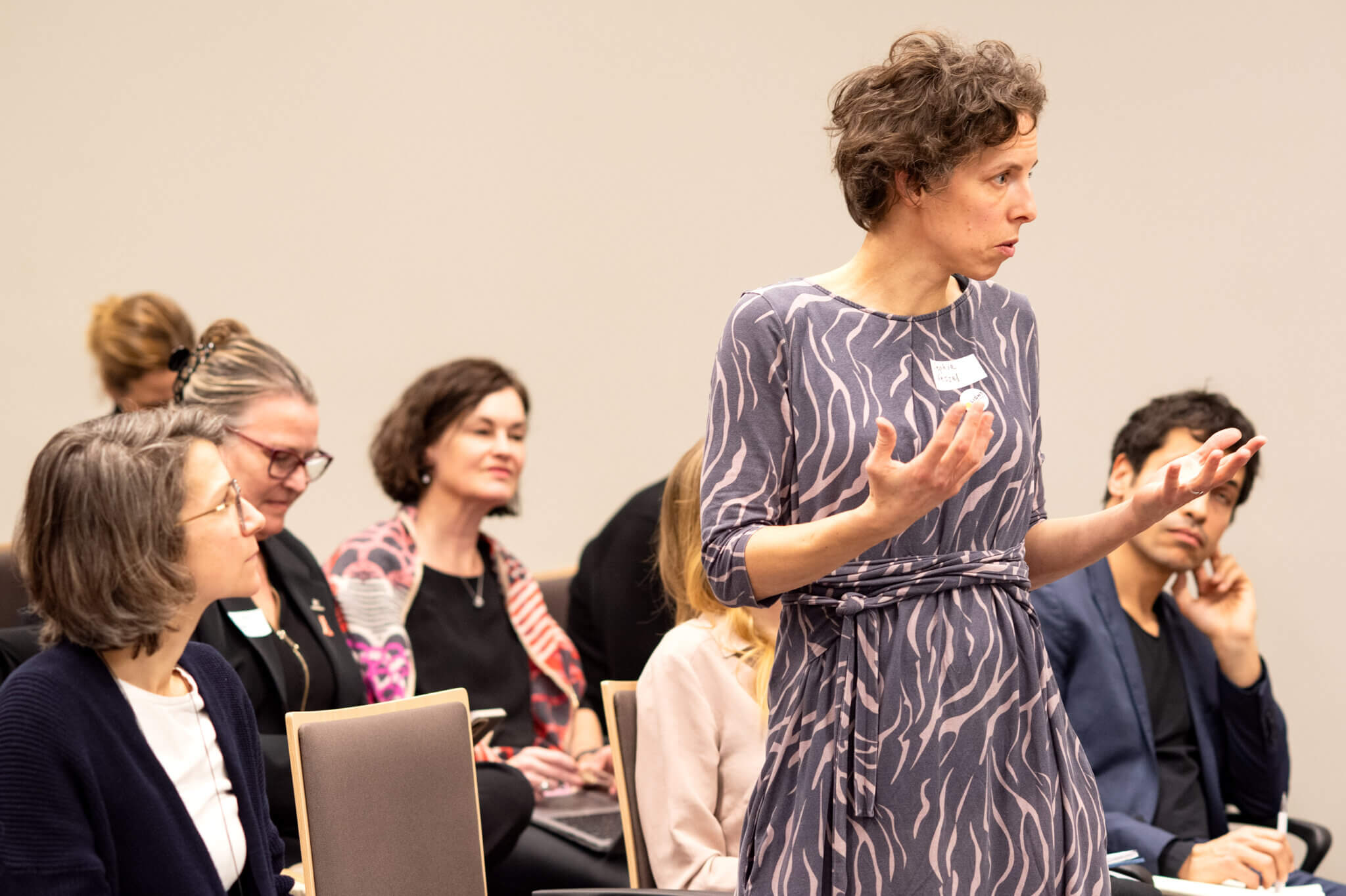 On the picture you can see a woman who is currently speaking to a audience in a panel discussion around humanitarian action. She is standing in front of the audience but currently talking backwards to the podium.