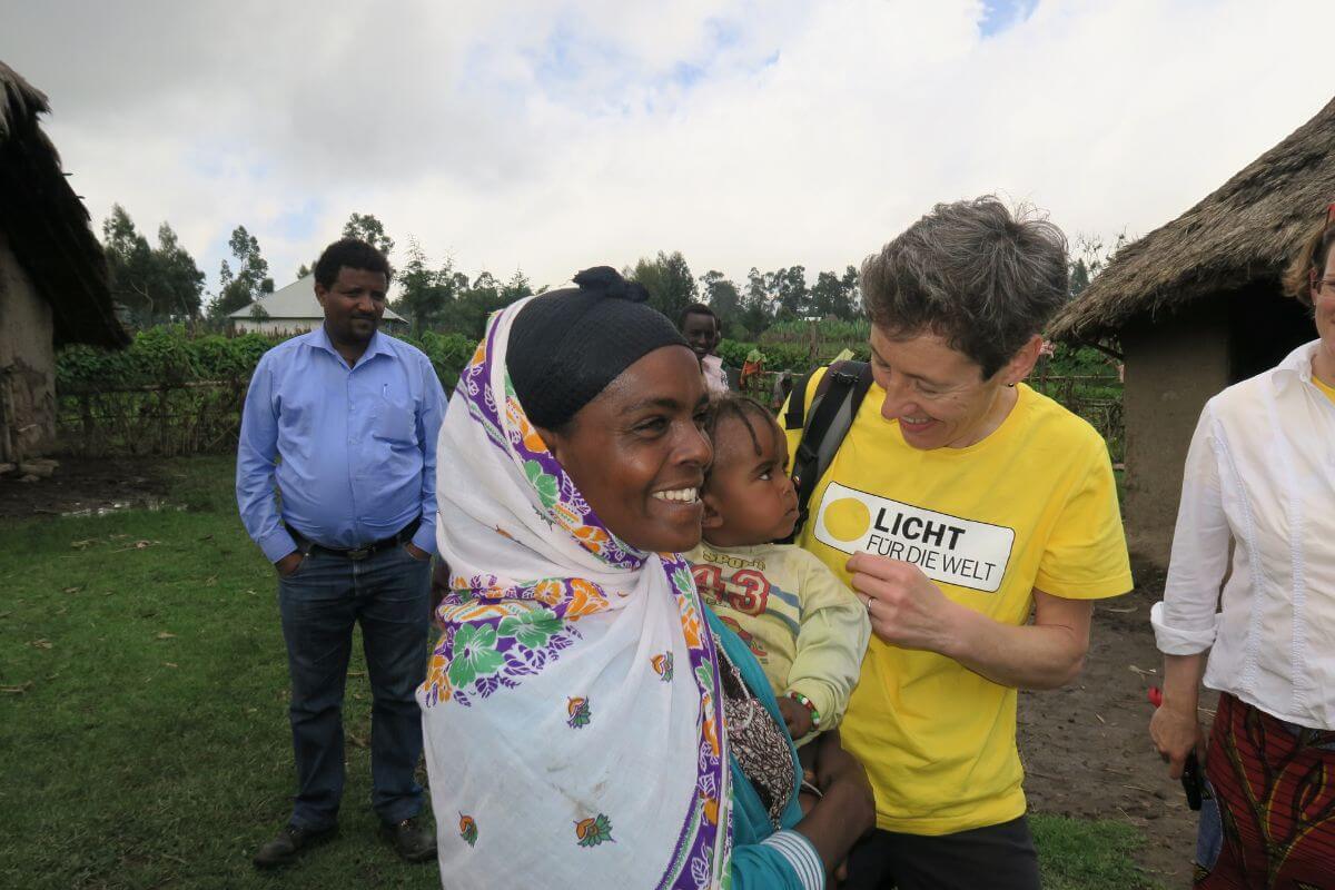 Johanna Mang lächelt bei einem Licht für die Welt Projektbesuch ein äthiopisches Baby an, das von seiner Mutter im Arm gehalten wird