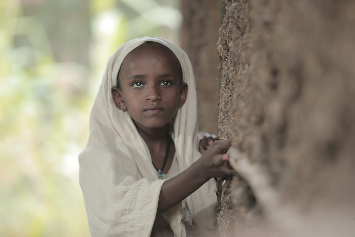 Auf dem Bild ist ein junges Mädchen zu sehen, dass sich an einer Wand entlang fortbewegt. Sie leidet an fortgeschrittenem Grauem Star und kann deshalb nur schwer ohne Hilfe alleine wohin gehen.