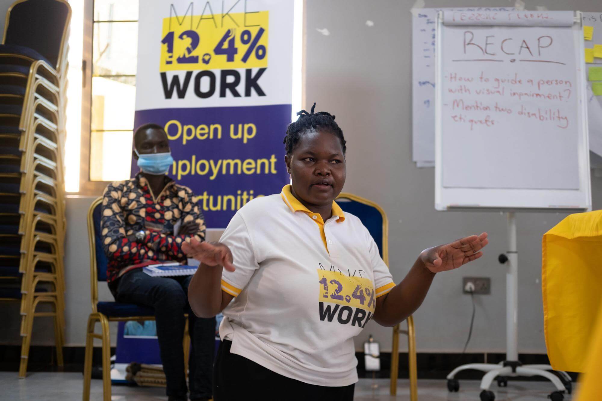 Das Bild zeigt Cony Adoch, Inklusionsexpertin bei Licht für die Welt. Sie hält einen Vortrag und trägt ein T-Shirt mit dem Logo der Initiative "Make 12,4 % work". Das Programm unterstützt Menschen mit Behinderung in Uganda, ihren Platz in der Berufswelt zu finden.