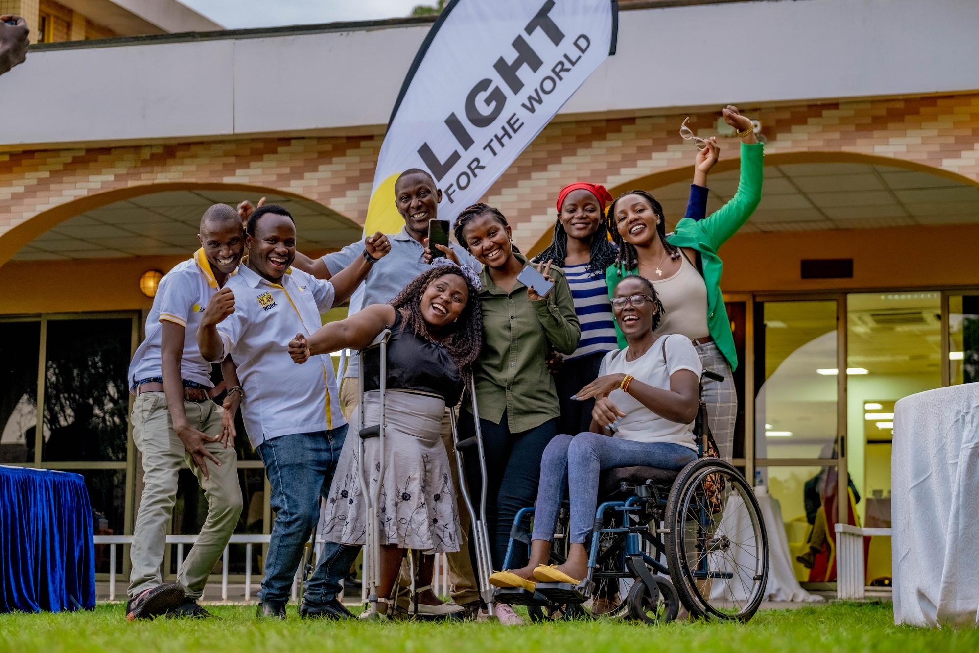 Acht Menschen mit Behinderungen in Uganda posieren mit glücklichen Gesichtern vor der Kamera. Sie stehen im Mittelpunkt und repräsentieren Licht der Welt und die Projekte der Organisation.