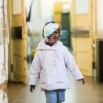 Deolinda, ein 2-jähriges Mädchen, läuft mit einem Verband über dem Auge lachend über den Krankenhausflur