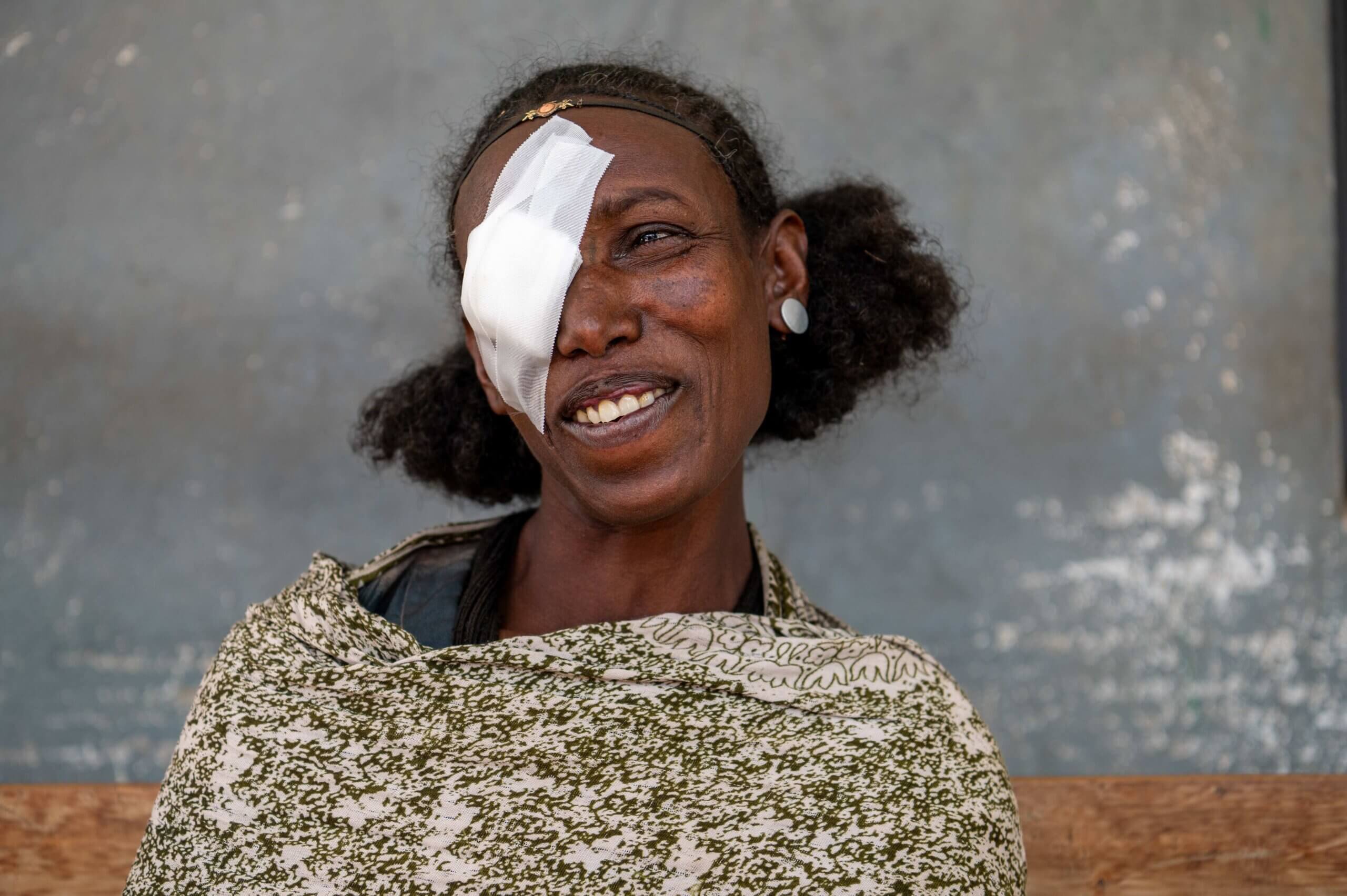 Auf dem Bild ist eine Frau mit einem Verband um das linke Auge zu sehen. Sie lacht und ist glücklich. Gerade wurde sie wegen der Augeninfektion Trachom operiert, die ihr Augenlicht gerettet hat.