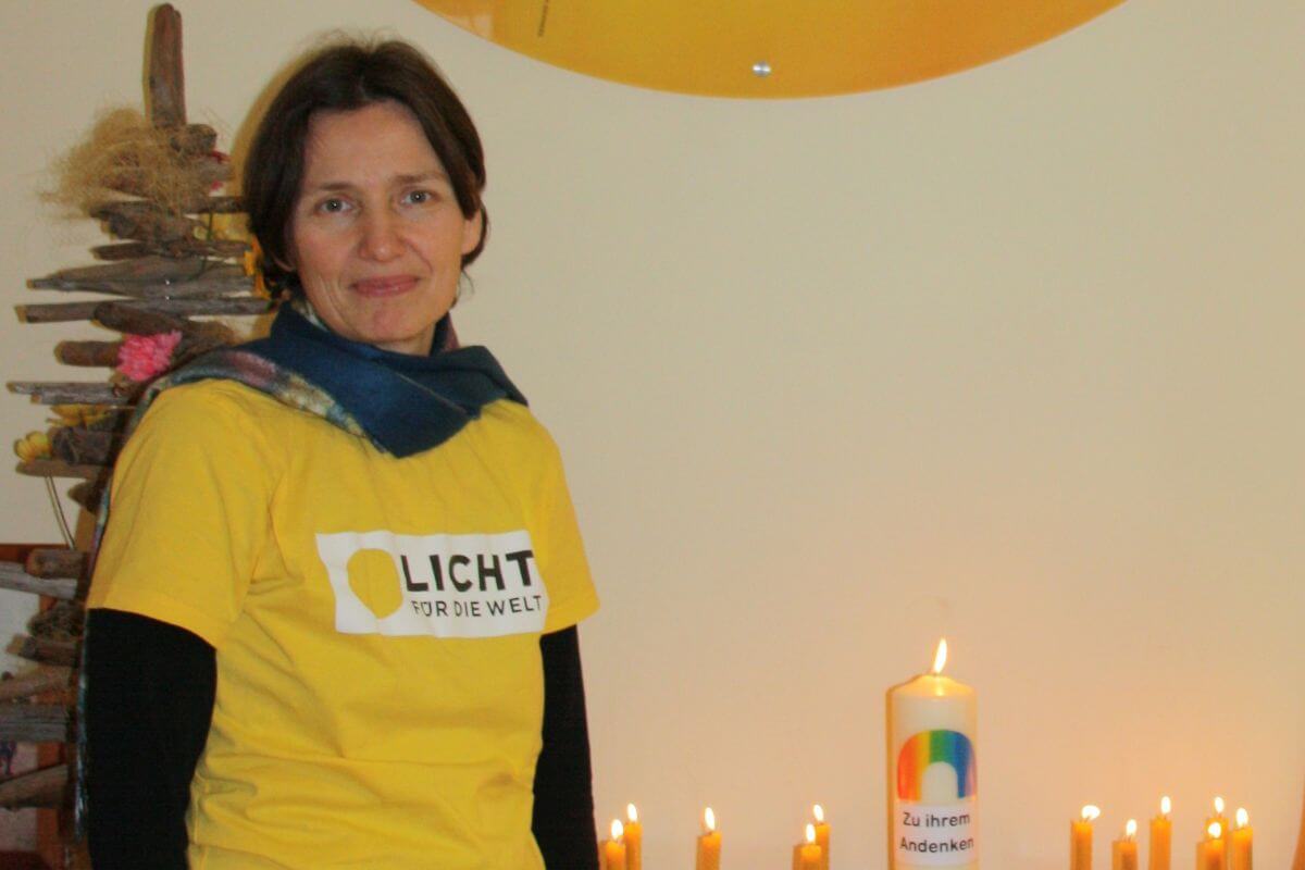Eva Dürr trägt ein gelbes T-Shirt mit Licht für die Welt Logo und lächelt in die Kamera. Neben ihr brennt eine Gedenkskerze
