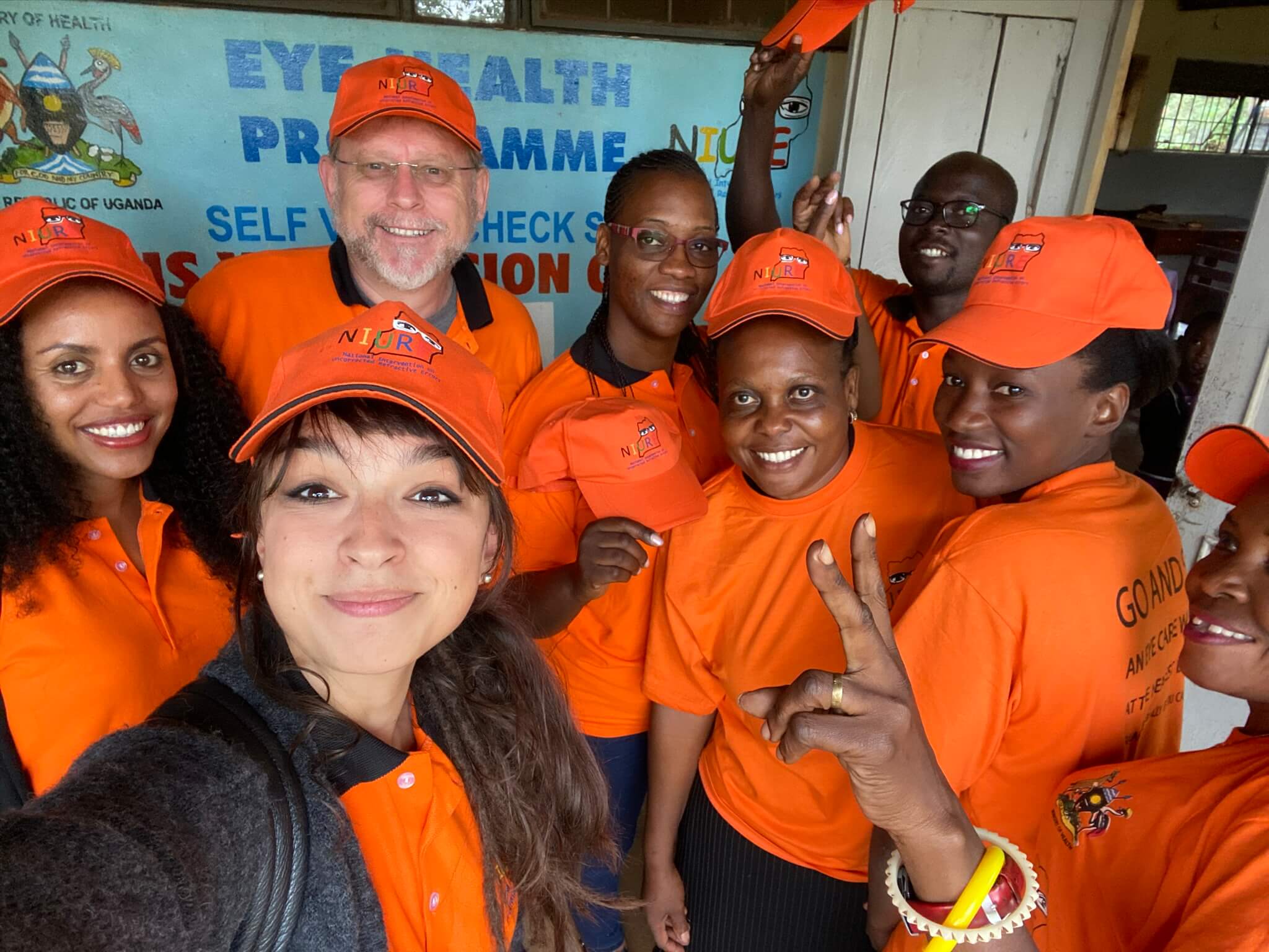 Flavia und Alem zusammen mit anderen Mitgliedern des Augengesundheitsteams von Licht für die Welt in Uganda. Alle tragen orangefarbene T-Shirts und Mützen