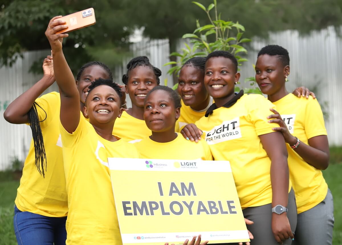 Sieben Frauen im gelben Licht für die Welt T-Shirt posieren für ein Foto mit dem Schild "I am employable"