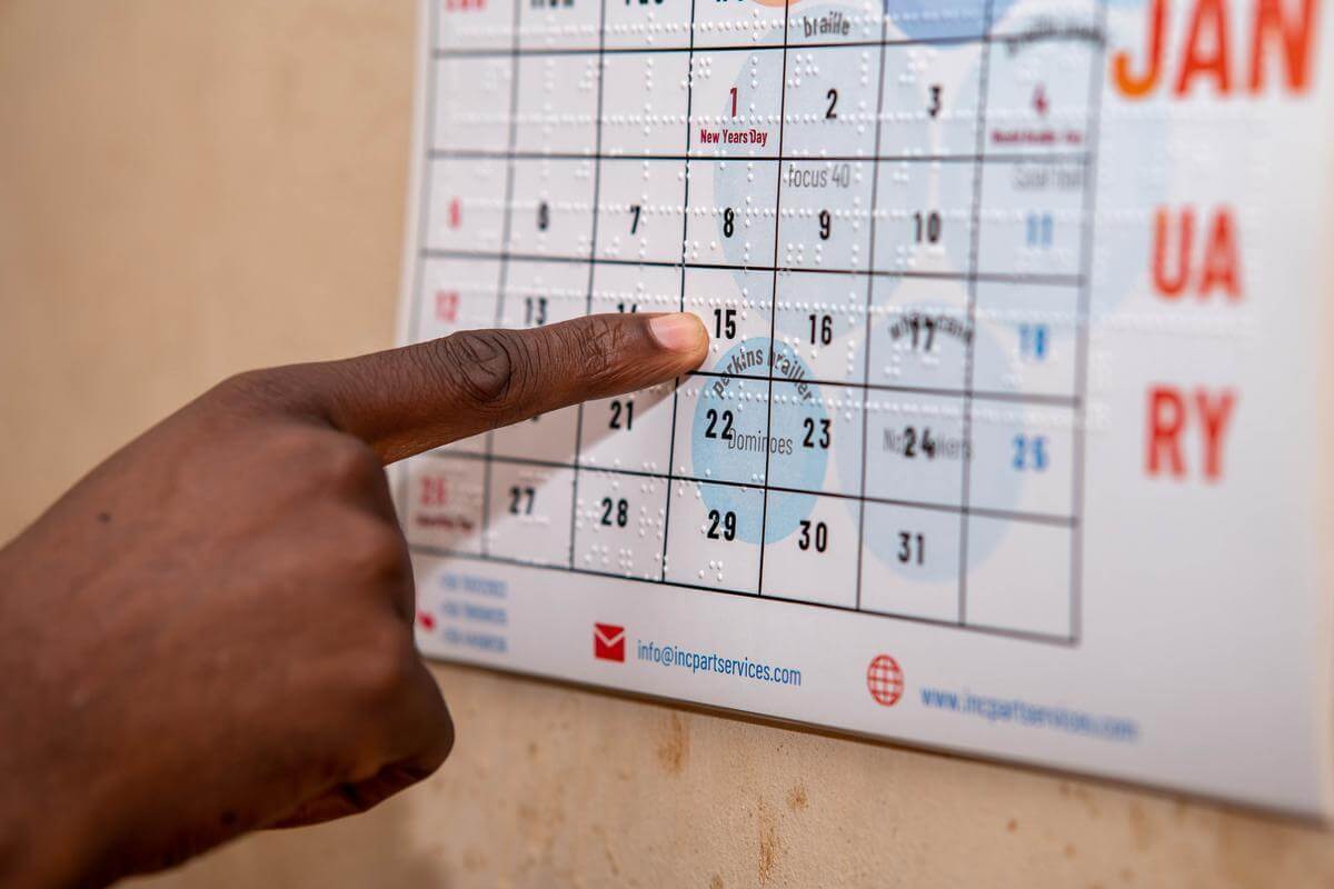Ein Mensch fährt mit seinem Finger über Braille-Schrift auf einem Kalender.