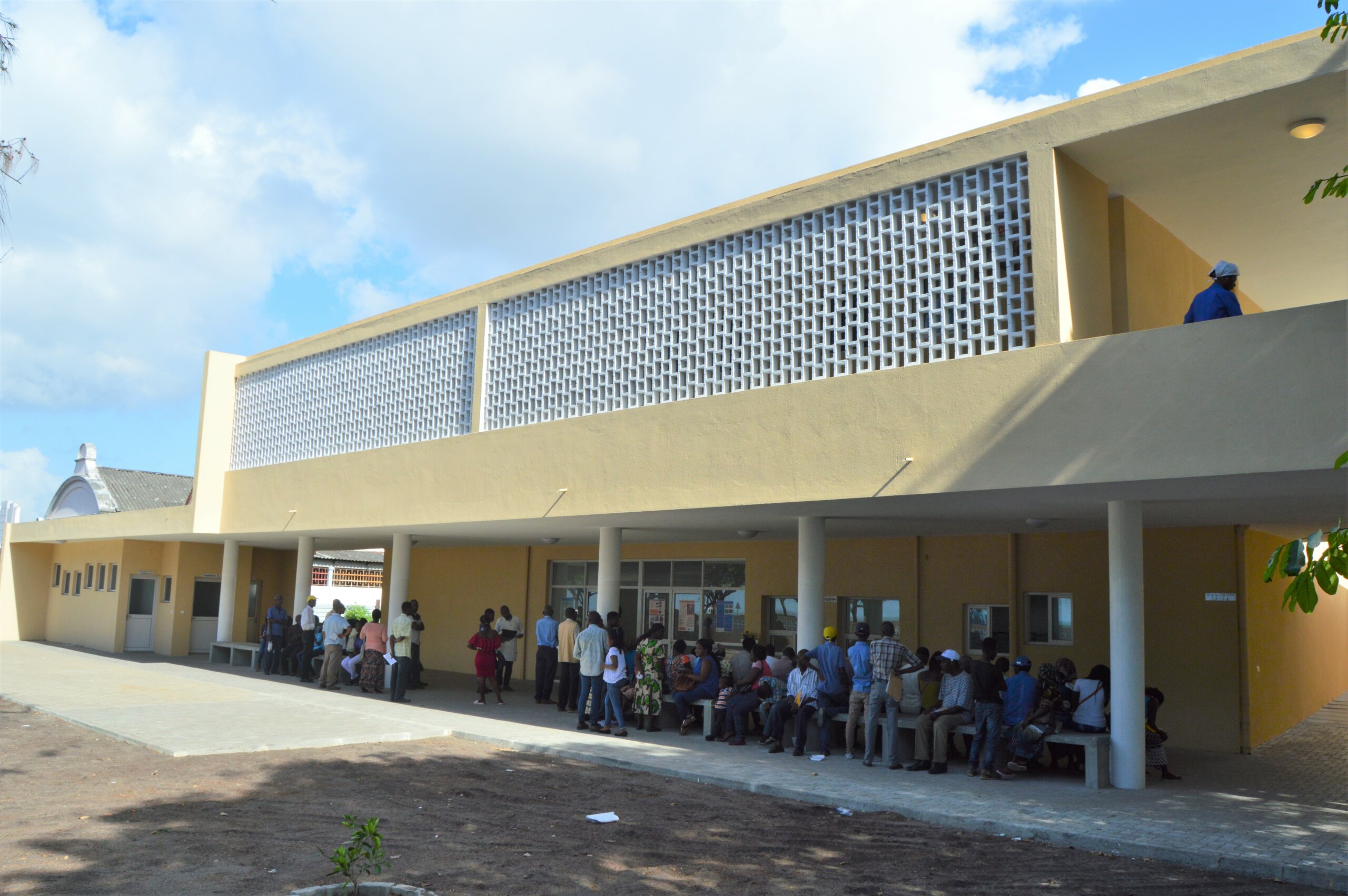 Auf dem Foto ist die Augenklinik in Beira, Mosambik zu sehen. Es ist ein gelbes Gebäude vor dem zahlreiche Menschen sitzen.