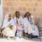 fünf Frauen sin hellen Gewändern sitzen in einer Reihe auf dem Boden und warten auf eine augenmedizinische Behandlung