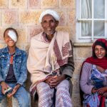 Ein äthiopischer Bursch sitzt neben seinem Vater und seiner Mutter. Alle lachen. Der Bub hat auf seinem linken Auge einen Verband.