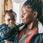 Eine Mutter aus Tansania hält ihr kleines Baby im Arm. Das Kind bekommt eine Augenoperatoin am Grauen Star.