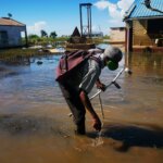 Ein alter Mann mit Krücken steht vor seinem überfluteten Haus im Südsudan.