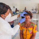 Eine Frau wird in einem Behandlungszimmer von einer Ärztin mit Mundschutz und Handschuhen am rechten Auge behandelt