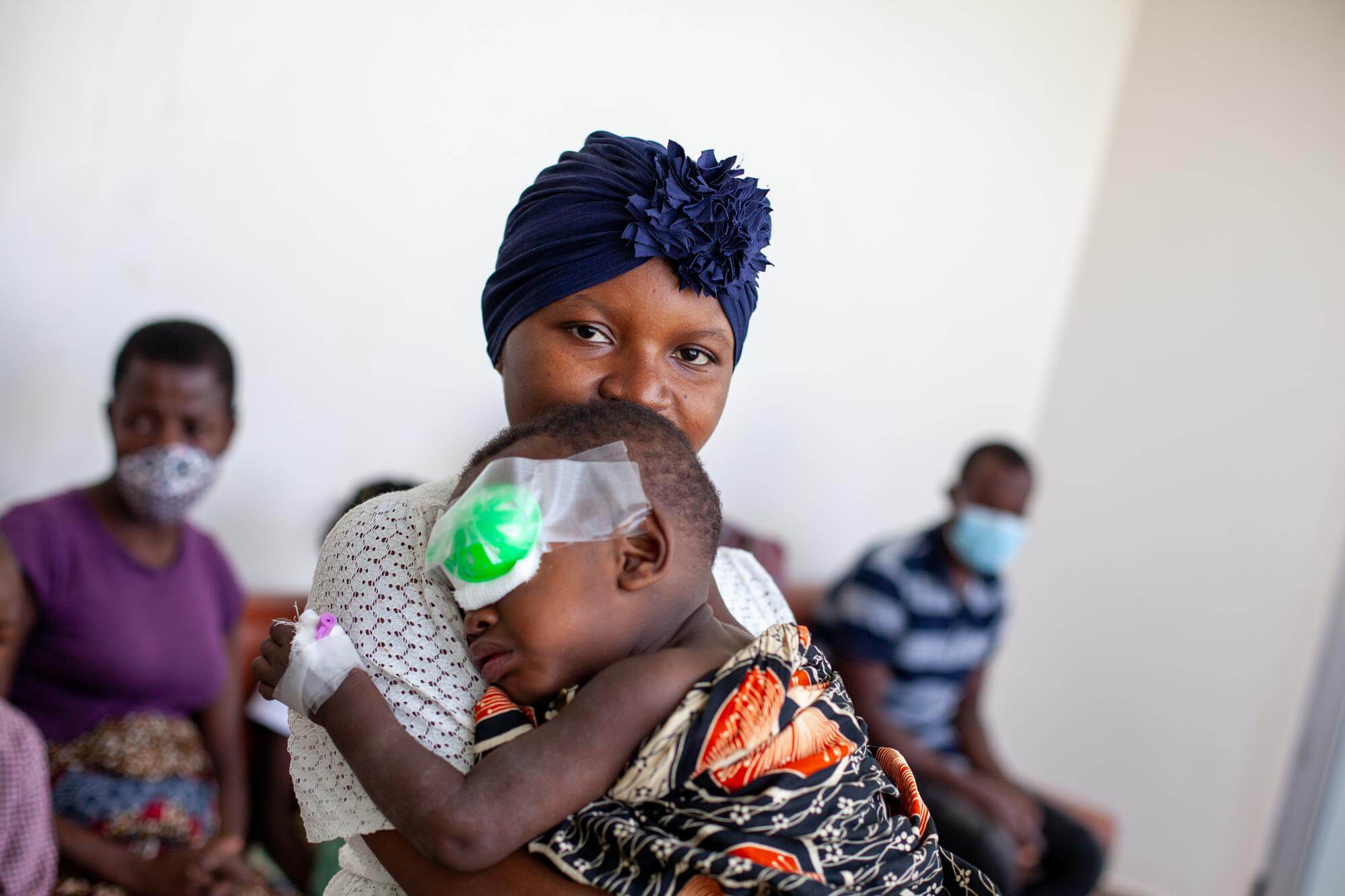 Nadja aus Mosambik hält ihren Sohn Ainyr in den Armen nachdem er am Grauen Star operiert wurde. Der kleine Bub hat einen Verband am linken Auge und ist in eine bunte Decke gewickelt.