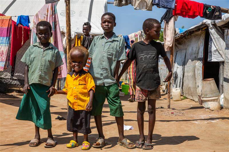 Ein kleines Mädchen mit Hydrozephalus lächelt und steht vor ihren drei Geschwistern.