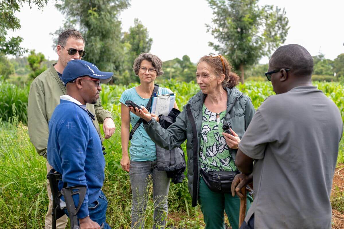 Elisa Vass, Ö1 Journalistin, interviewt David Ndungu auf einem Feld, während die restlichen Reisebegleiter*innen zusehen