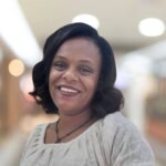 Porträt von Rediet Mesfin, eine Frau mit schulterlangen, gelockten dunklen Haaren und einem strahlenden Lächeln