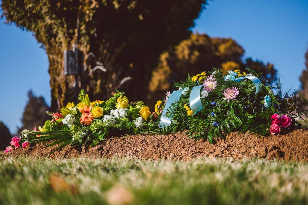 Zwei Blumenkränze liegen auf der Erde vor einem Baum - ein Symbolbild für eine Beisetzung im Garten