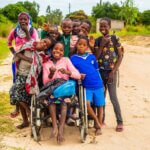 Ein Diashow-Bild zeigt eine große Gruppe von Kindern mit und ohne Behinderungen, die für ein Bild zusammenkommen und für das Bild posieren und lächeln.