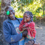 Franciscu aus Mosambik hält sein lachendes Enkelkind am Arm