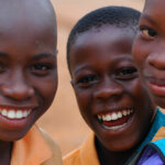 Drei Jugendliche blicken lächelnd in die Kamera. Sie tragen alle ein orangenes Hemd.