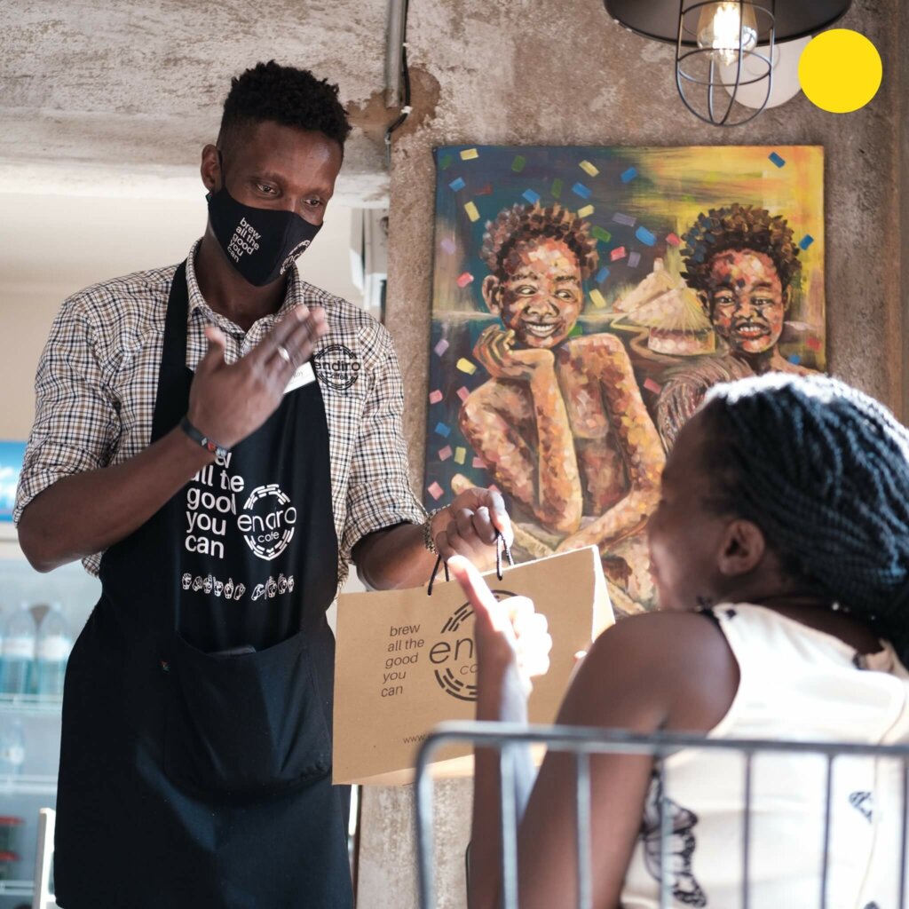 Ein junger Kellner spricht in Gebärdensprache mit einer Kundin des Gebärdensprachencafés in Uganda.