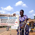 Jenny, die 2021 ihr eigenes Reinigungsunternehmen gegründet hat, steht neben einem Schild, das ihr Unternehmen bewirbt.