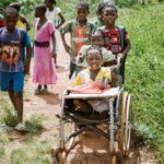 Eine Gruppe Kinder ist auf dem Heimweg von der Schule. Ein Mädchen im Rollstuhl wird von den anderen Kindern nach Hause geschoben.