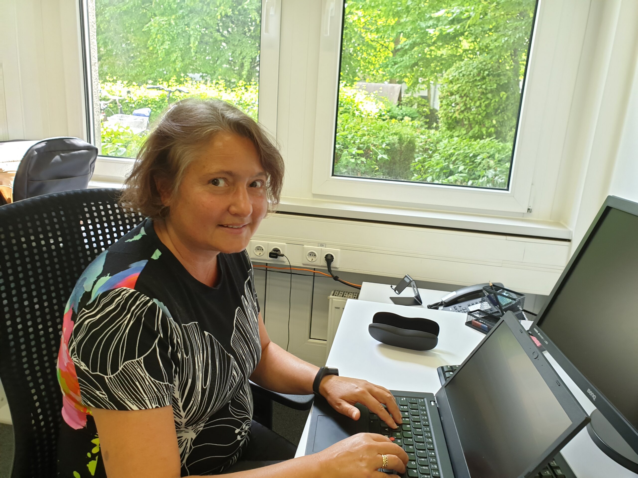 Ehrenamtliche Kirsten sitzt am Schreibtisch vor dem Laptop und lächelt in die Kamera