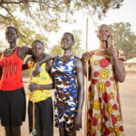 Vier Frauen aus dem Südsudan in bunter Kleidung stehen nebeneinander und blicken selbstbewusst in die Kamera.