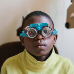 Ein Junge aus Uganda sitzt auf einem Sessel und trägt ein Gerät, das dem Optiker dabei hilft, die richtige Sehschärfe für die Brille des Jungen herauszufinden.