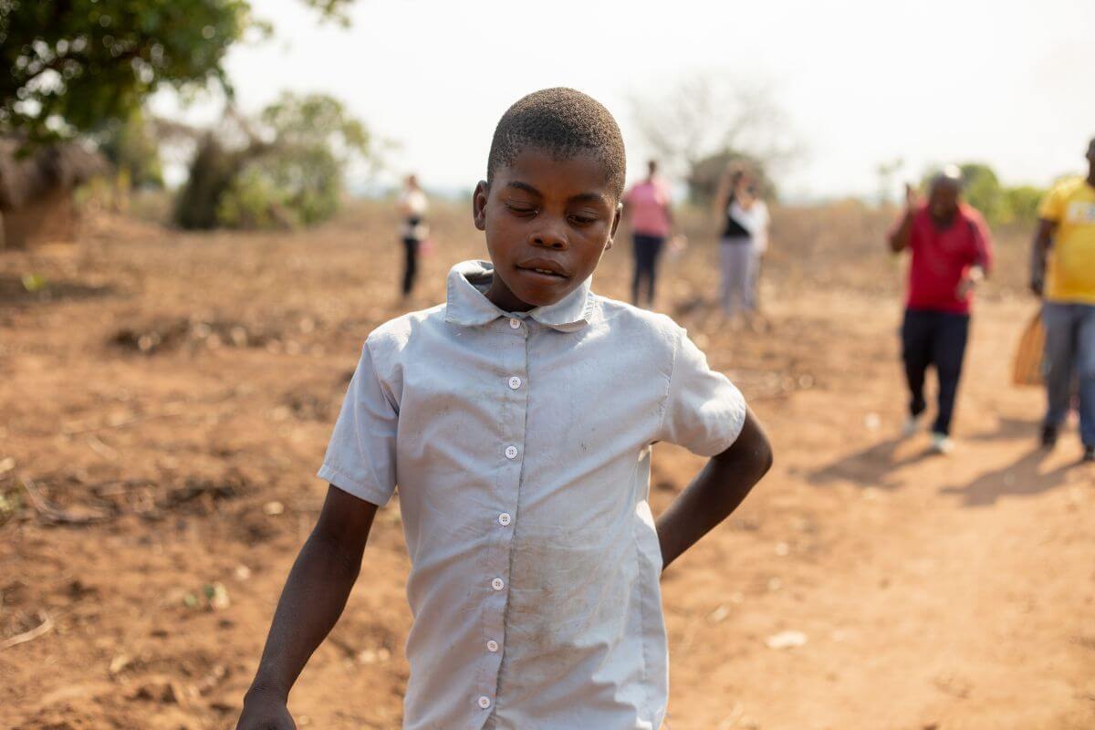 Ministro, ein 12-jähriger Junge aus Mosambik, zu sehen auf der Straße in seinem Heimatdorf. Er trägt ein graues Hemd und sieht zu Boden