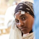 Tsega, eine 23-jährige Frau, blickt ernst in die Kamera. Sie trägt ein schwarzes Tuch und Markierungen über den Augen