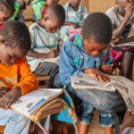 Kinder sitzen in einem Klassenraum und haben Schulhefte vor sich.