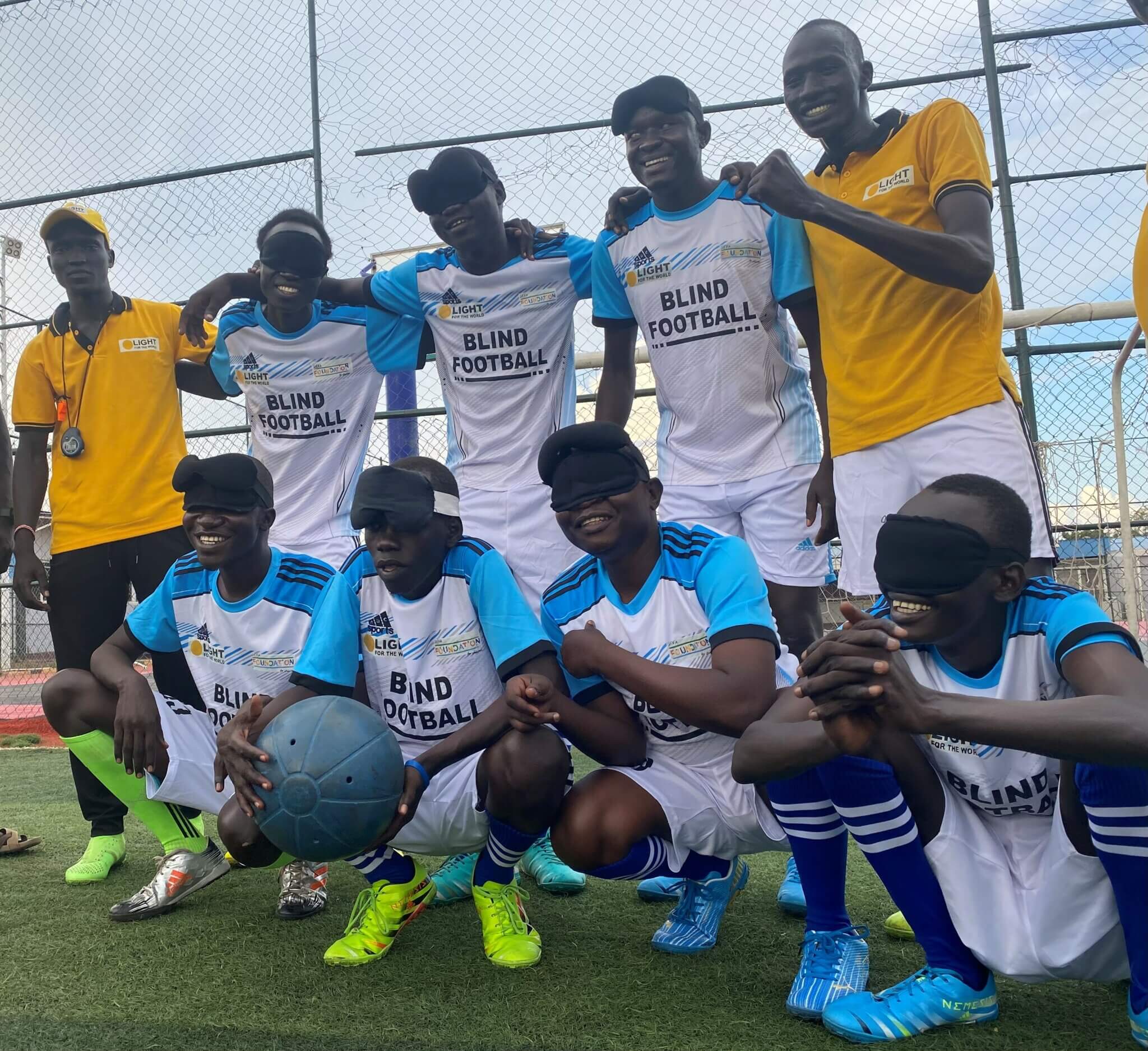 Zu sehen ist die Fußballmannschaft des blinden Fußballvereins im Südsudan. Die Spieler tragen Augenbinden und einer hält den Spielball. Simon, der Trainer, ist ebenfalls auf dem Bild.