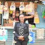 Eine Frau im schicken schwarzen Business-Kostüm steht vor Ihrem Geschäft in Nairobi