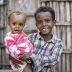 Ein kleiner Junge lächelt, während er seine kleine Schwester trägt.