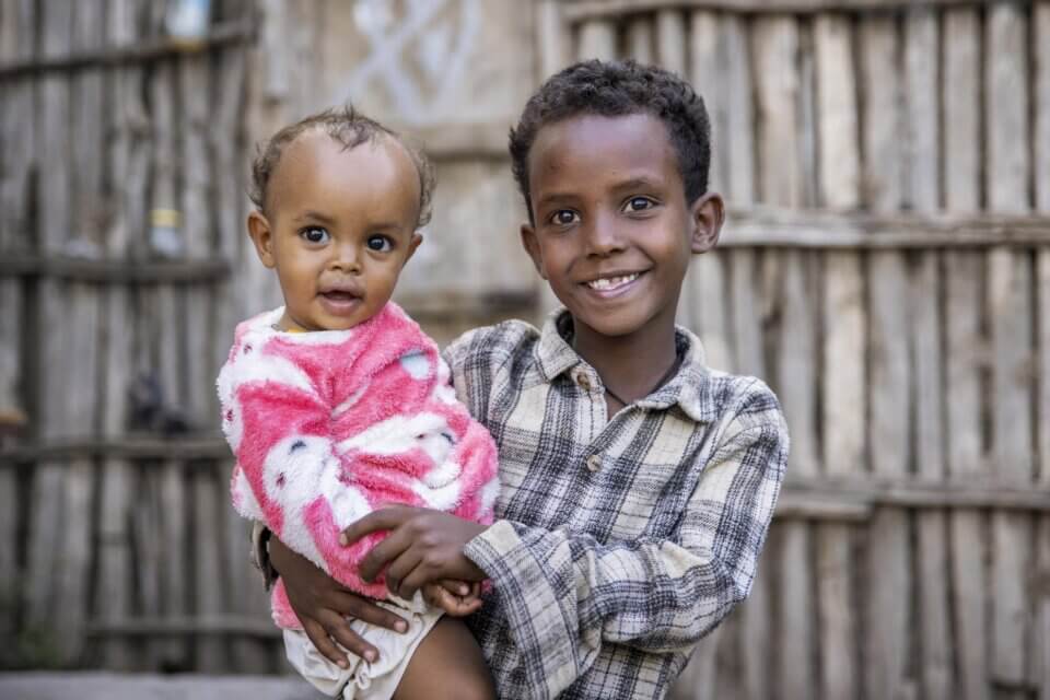 Ein kleiner Junge lächelt, während er seine kleine Schwester trägt.
