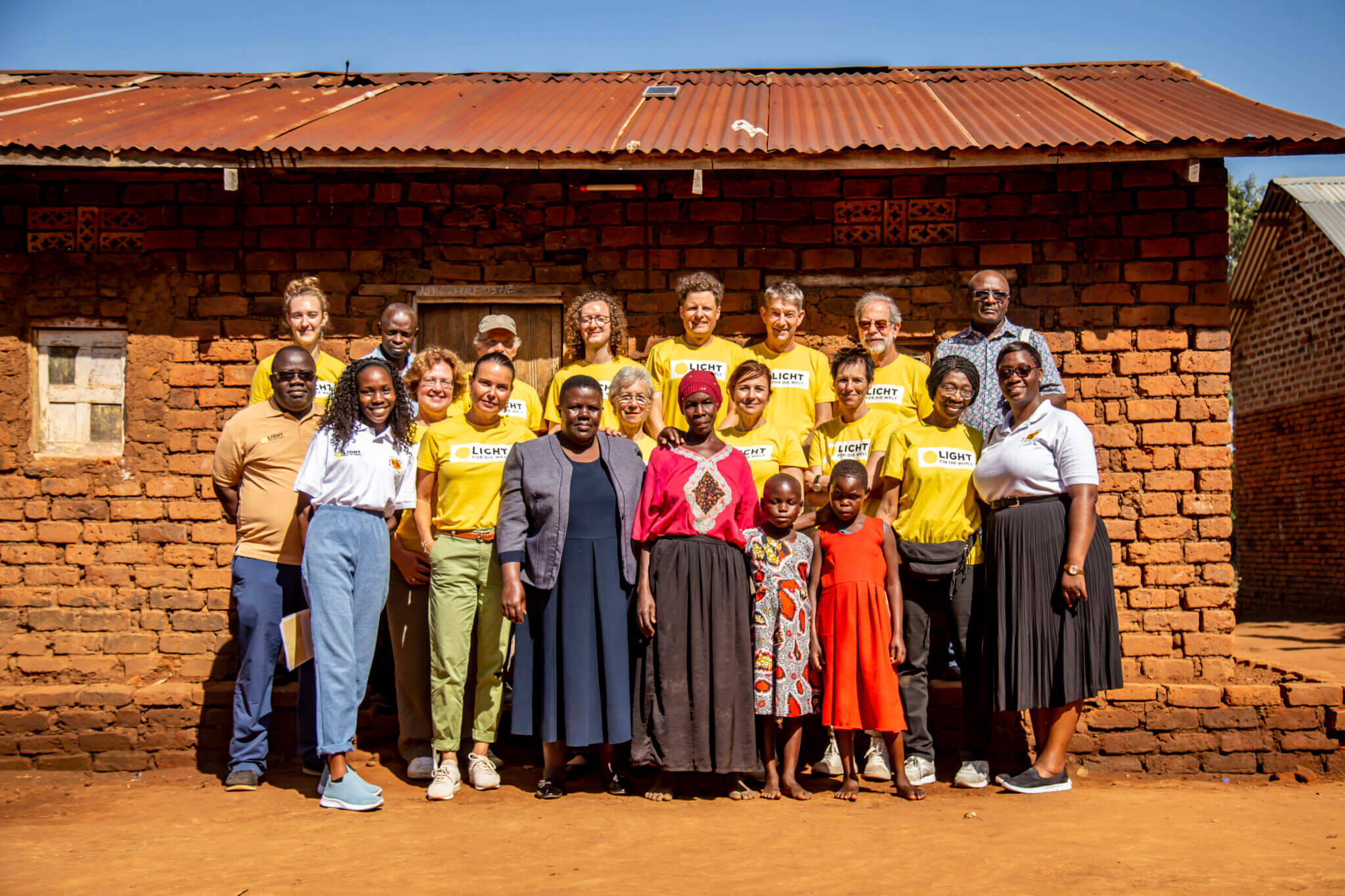 Gruppenfoto in Kikubo, Uganda. Auf dem Foto sind Menschen aus dem Dorf zu sehen, unter anderem zwei lokale augenmedizinische Fachpflegekräfte, sowie Mitarbeitende von Light for the World und Augenärzte aus Deutschland, Österreich und der Schweiz
