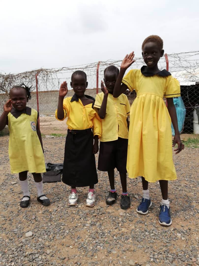 Vier Mädchen in gelben Schuluniformen stehen vor einem Stacheldrahtzaun. Sie leben im Camp für Binnengeflüchtete Mangateen.