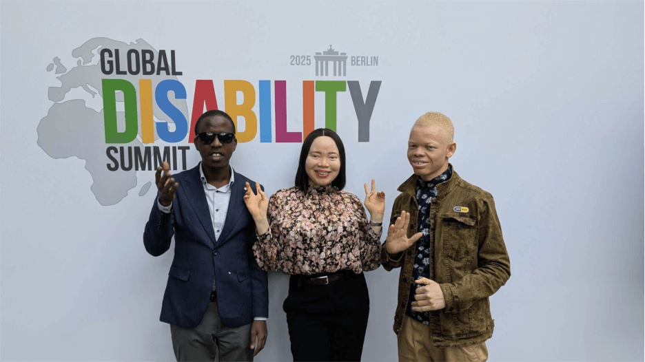 Drei junge Menschen mit Behinderungen - zwei Burschen und ein Mädchen - grinsen in die Kamera. Sie nahmen am Global Disability Summit teil.