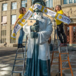 Licht fü rdie Welt zetzt ein Zeichen in der Schweiz und verdeckt die Augen einer Statue mit einem gelben Banner.
