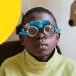 Ein Junge aus Uganda sitzt auf einem Sessel und trägt ein Gerät, das dem Optiker dabei hilft, die richtige Sehschärfe für die Brille des Jungen herauszufinden.