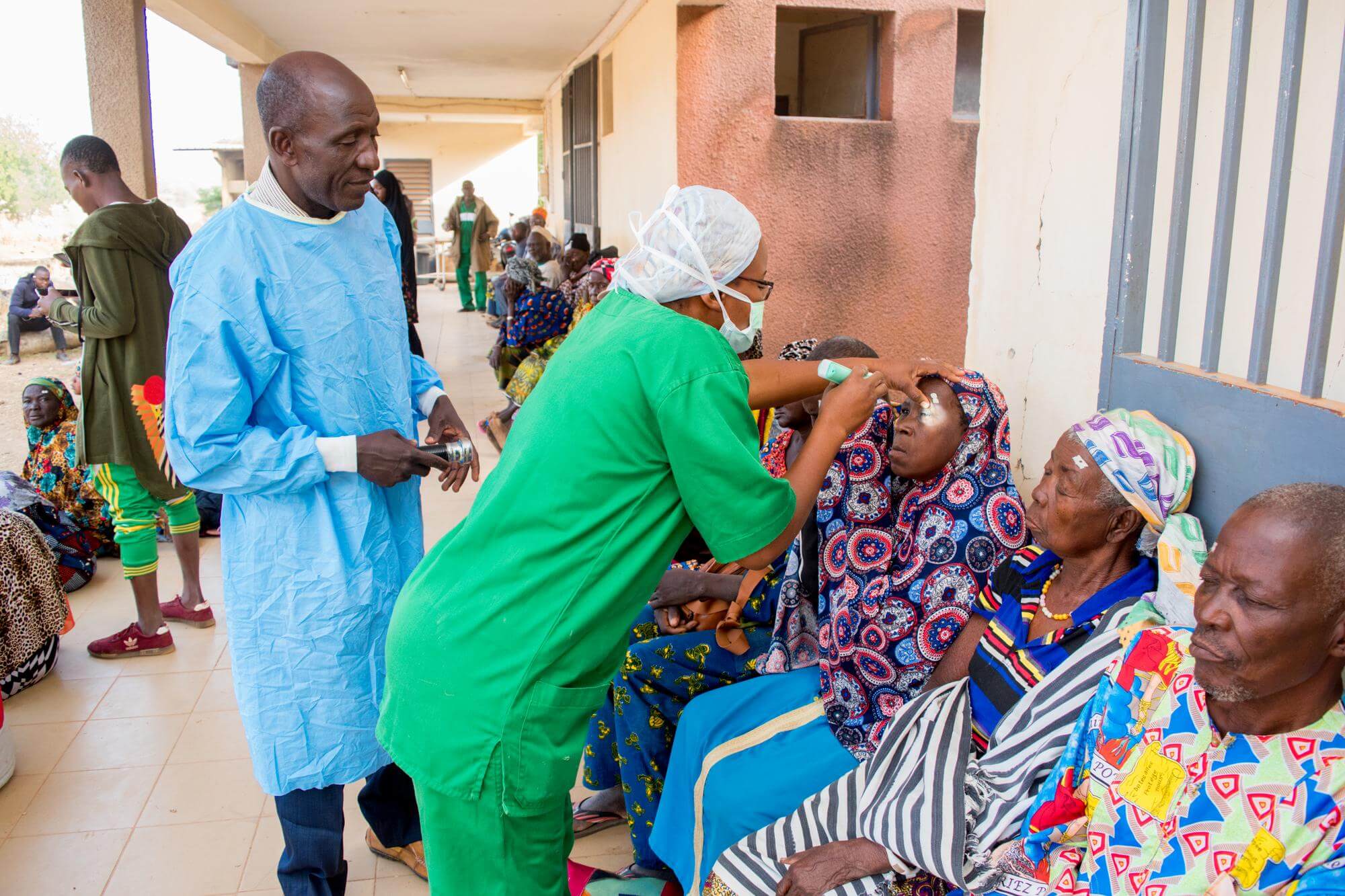 Eine Krankenpflegerin in einem grüner OP-Kleidung untersucht die Augen von Frauen, die bei einem mobilen Einsatz operiert werden sollen. (c) KIO Photography