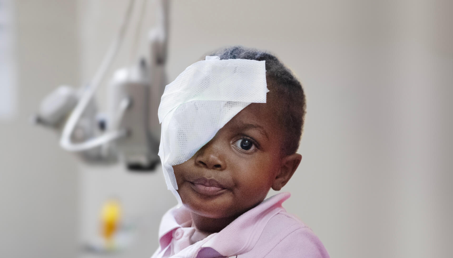 Nahaufnahme des 2-jährigen Mädchens Deolinda im Spital. Sie blickt in die Kamera und hat einen Verband über dem rechten Auge.