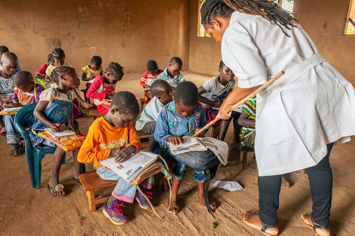 Eine Lehrerin unterrichtet Kinder in einer inklusiven Schule in Mosambik im Jahr 2022 . Die Schüler schauen auf ihr Lehrbuch, während die Lehrerin ihnen etwas zeigt.